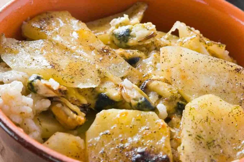 Tradycyjna apulijska zapiekanka tiella barese z ryżem, ziemniakami i ołżami w glinianym naczyniu.