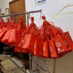 Bright red Calici nel Borgo Antico wine bags hanging on a rack in Bisceglie, ready for visitors to use during the festival’s wine tastings.