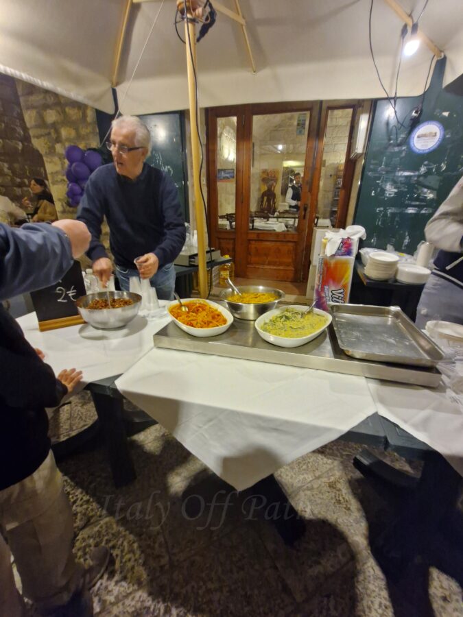 Local vendor serving plates of homemade pasta at a street food stand during Calici nel Borgo Antico in Bisceglie’s old town.