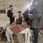 A sommelier serving wine at a tasting table during Calici nel Borgo Antico in Bisceglie, with visitors sampling different bottles in the old town.