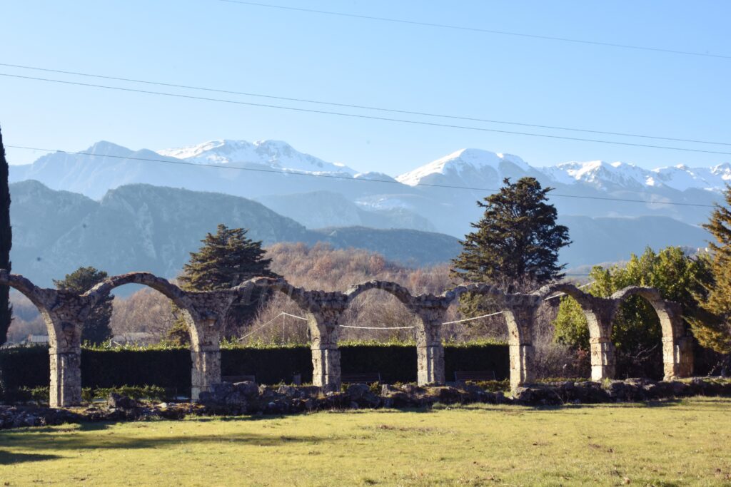 Stone arches of the San Vincenzo al Volturno monastery ruins with snow-covered mountains in the background on a sunny winter day.