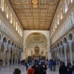 „Wnętrze bazyliki Sant’Apollinare Nuovo w Rawennie – długa nawa z kolumnadą i słynnymi bizantyjskimi mozaikami ukazującymi procesję świętych.