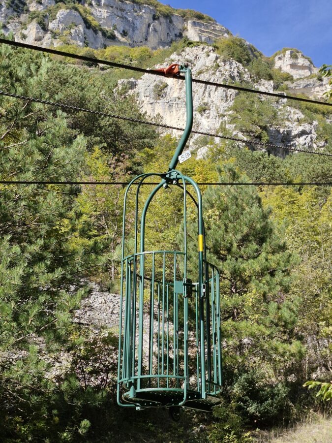 Historic open-air cable car basket of Grotta del Cavallone in Abruzzo, Italy, surrounded by rocky mountains and pine trees.