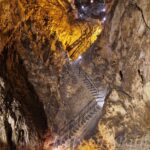 Illuminated stairway inside Grotta del Cavallone in Abruzzo, Italy, showing steep rocky walls and dramatic cave lighting