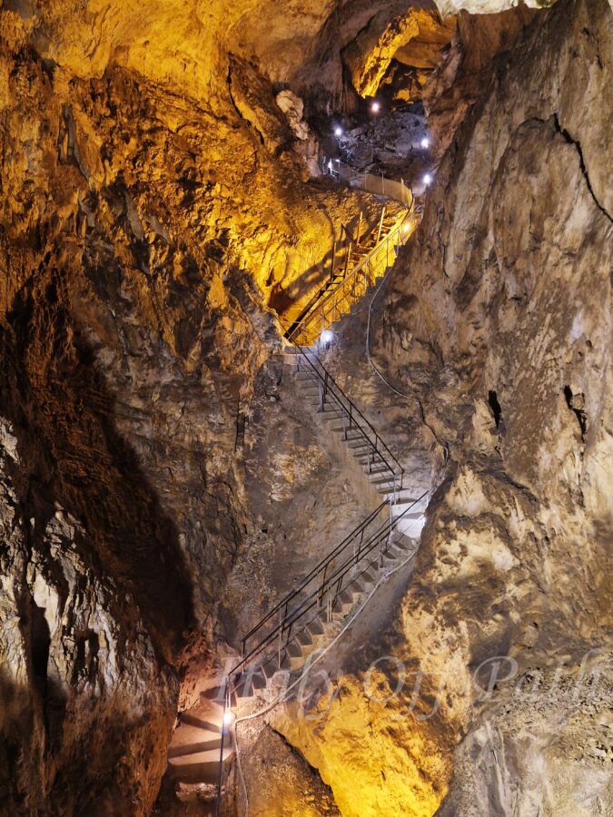 Illuminated stairway inside Grotta del Cavallone in Abruzzo, Italy, showing steep rocky walls and dramatic cave lighting