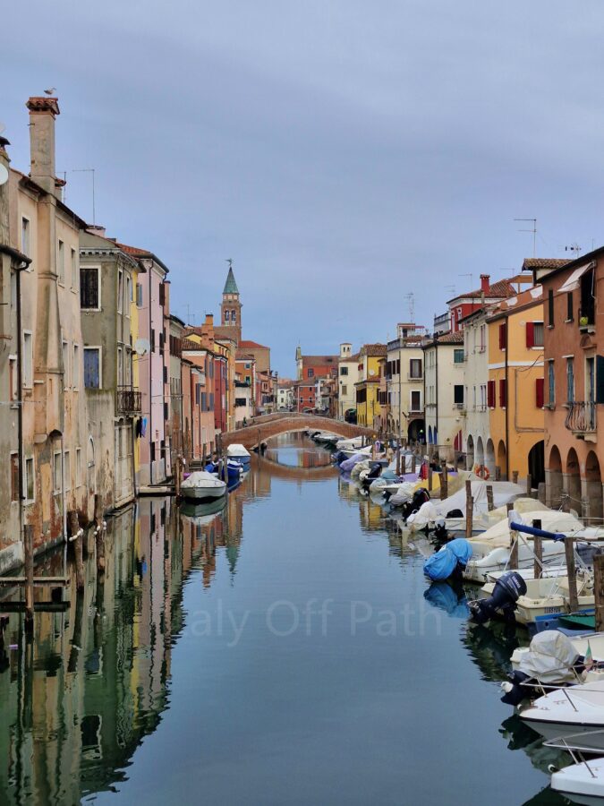 Visiting Chioggia. A water canal in Chioggia lined with multi-colored houses and moored boats under an overcast sky