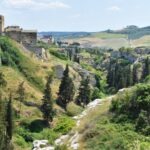 View from the edge of Gravina di Puglia overlooking the steep green canyon with ancient stone houses and cypress trees
