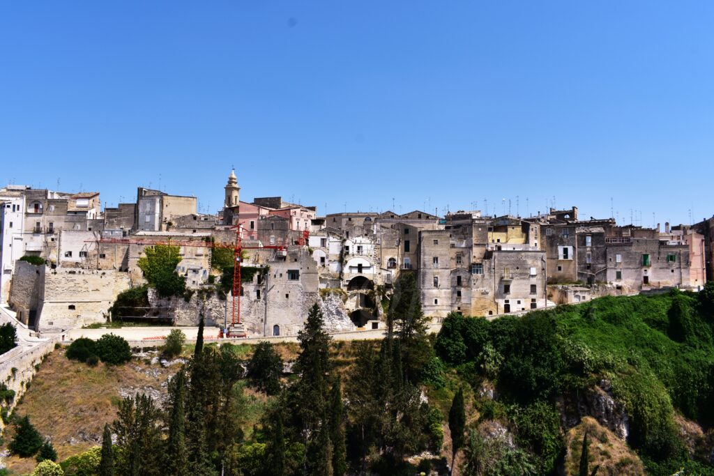 Wide panoramic view of the Gravina di Puglia old town skyline perched on a limestone cliff with a bright blue sky