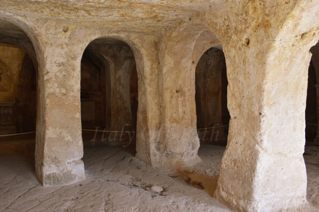 Interior of a cave church in Gravina di Puglia featuring ancient stone pillars and arches carved directly out of the limestone rock