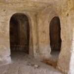 Interior of a cave church in Gravina di Puglia featuring ancient stone pillars and arches carved directly out of the limestone rock
