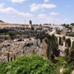 Panoramic view of the Ponte Acquedotto bridge and the rock-cut caves of the Gravina di Puglia canyon under a blue sky