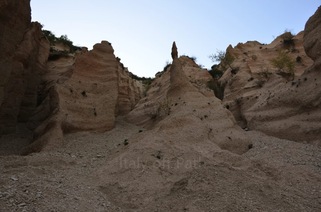 A close-up view of the eroded red gravel towers and rock formations at Lame Rosse, showing the detailed texture of the layered earth and a central sharp pinnacle against a bright sky.