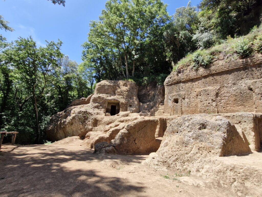 The wide exterior facade of the ancient Etruscan Tomba della Regina (Queen's Tomb) carved out of a massive yellow tufa rock face on the Three Villages Trail.