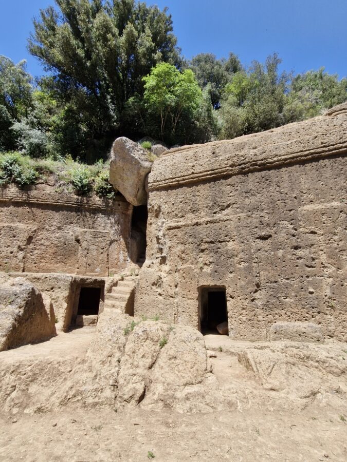 A closer view of the large, square entrance and cut-out architectural chambers of the ancient Tomba della Regina monumental rock tomb in Lazio.