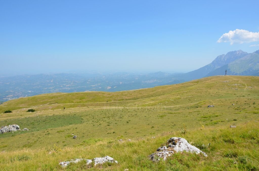 Croce di Arapietra summit cross standing on a vast grassy mountain ridge overlooking the surrounding valleys and peaks in Gran Sasso, Abruzzo, Italy.