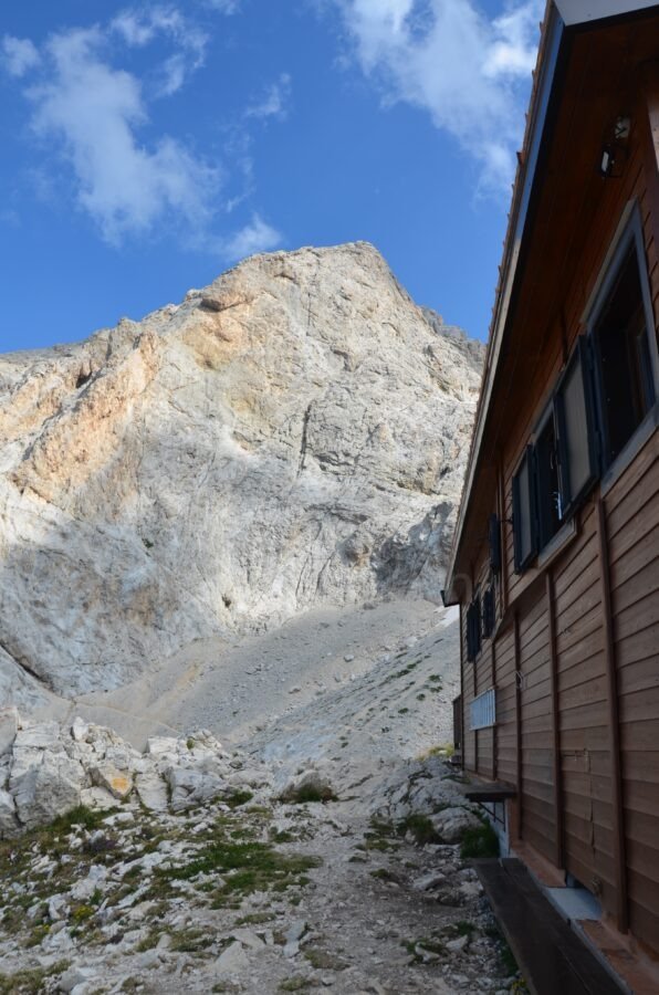 View of the towering rocky peak of Corno Grande from the wooden wall of Rifugio Franchetti in Gran Sasso, Abruzzo, Italy.