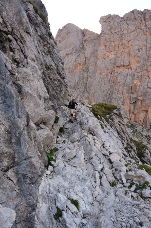 Hiker with trekking poles descending a steep, rocky trail along a mountain cliff in Gran Sasso, Abruzzo, Italy