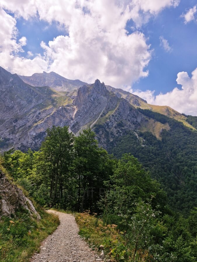 Narrow gravel mountain path winding toward Cascata Rio Arno with rugged peaks in Prati di Tivo, Abruzzo, Italy
