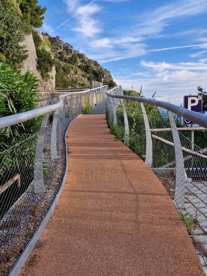 Paved pedestrian path with curved metal safety railings along the cliffside road near Maratea, Basilicata.