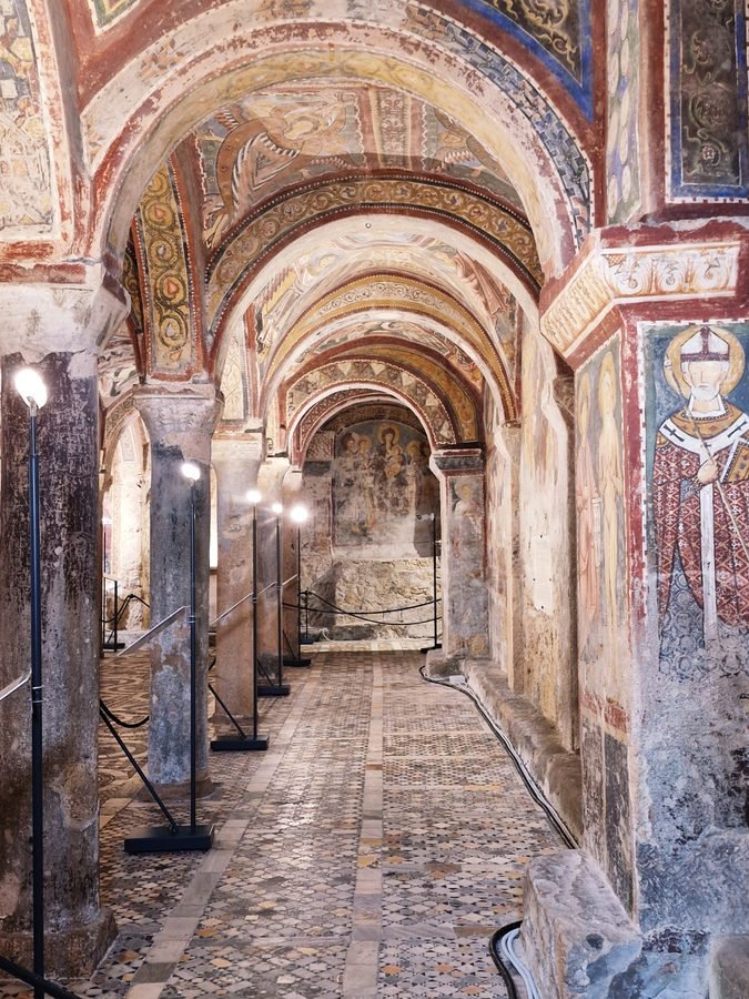 Vaulted aisle lined with Romanesque arches, medieval frescoes, and Cosmatesque mosaic floor in the Crypt of St Magnus, Anagni Cathedral, Lazio, Italy.