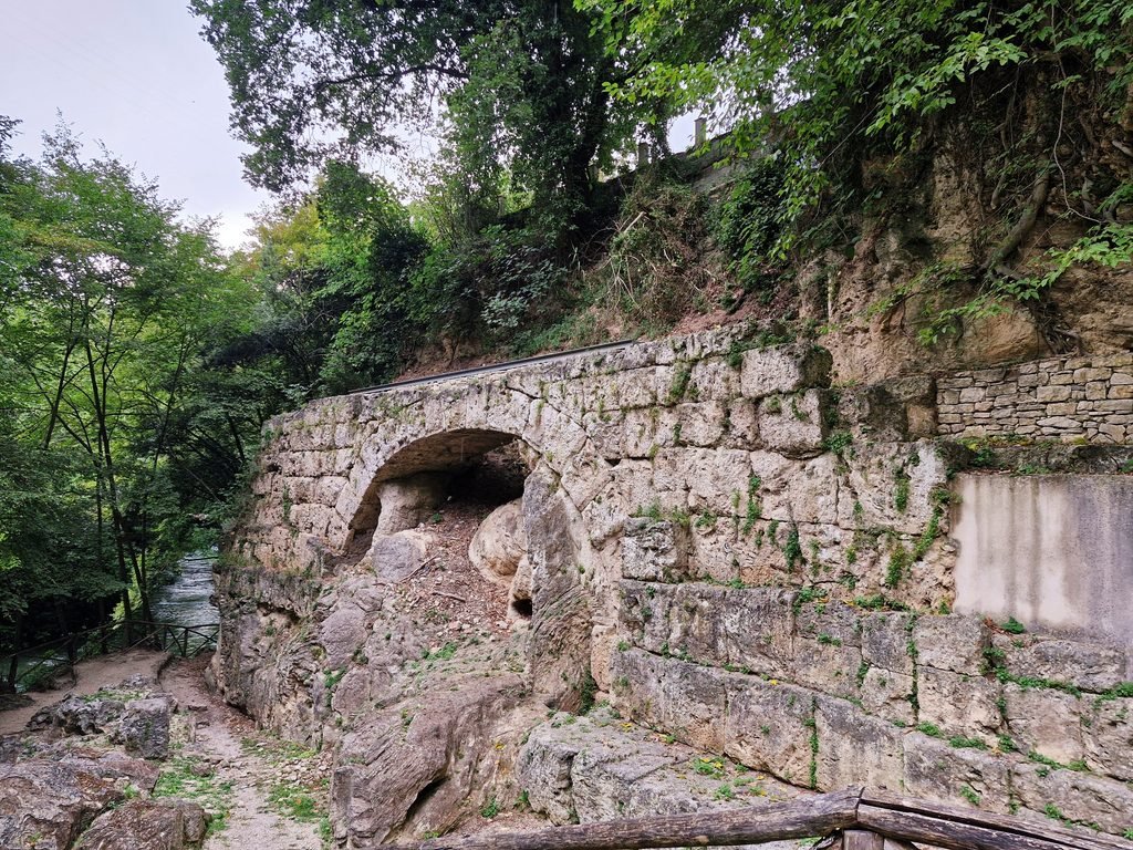 Ancient Roman stone arch of Ponte del Toro built against the rocky hillside next to a stream near Cascata delle Marmore, Umbria, Italy.