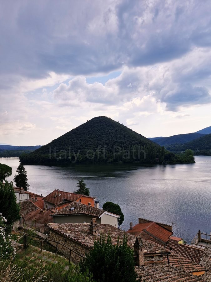 Rooftops of Piediluco village overlooking the lake toward the cone-shaped Mount Caperno under a dramatic cloudy sky, Umbria, Italy.