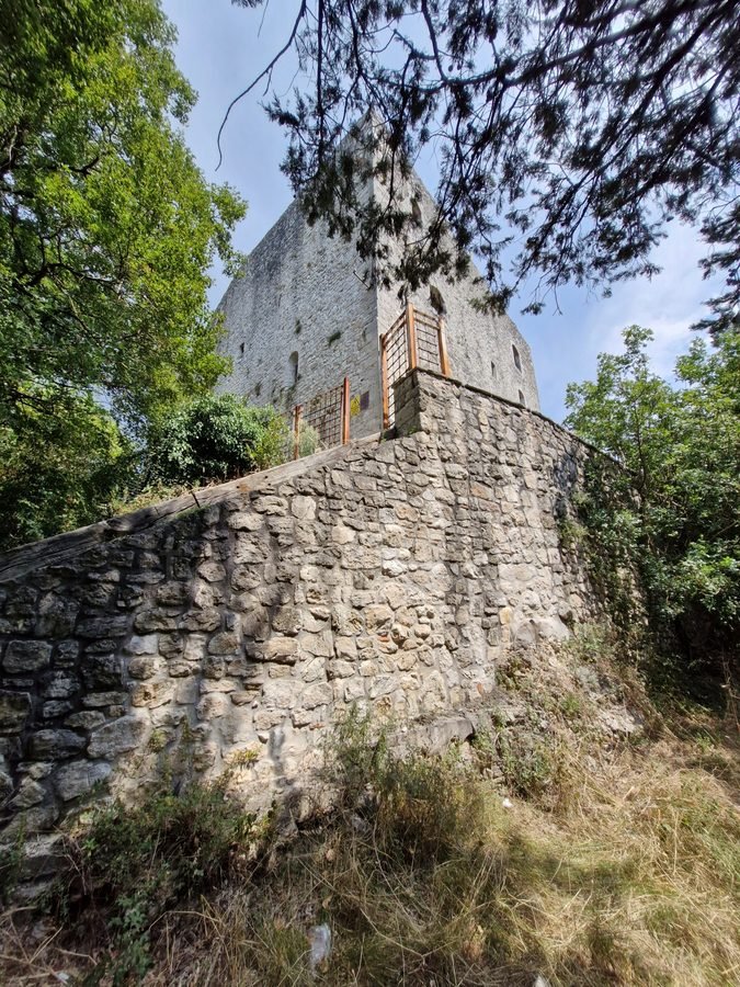 Low-angle view of the stone rampart and fortress tower of Rocca Albornoz surrounded by trees overlooking Lake Piediluco, Umbria, Italy.