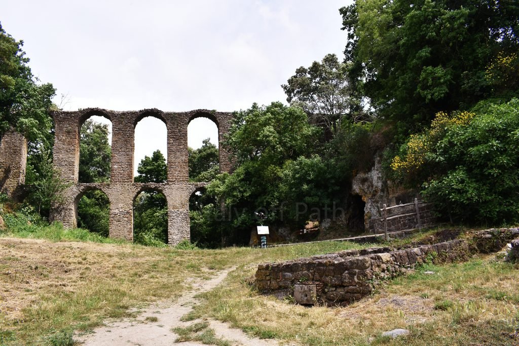 Ruins of a Roman-style arched aqueduct surrounded by trees in the ghost town of Antica Monterano, Lazio, Italy.