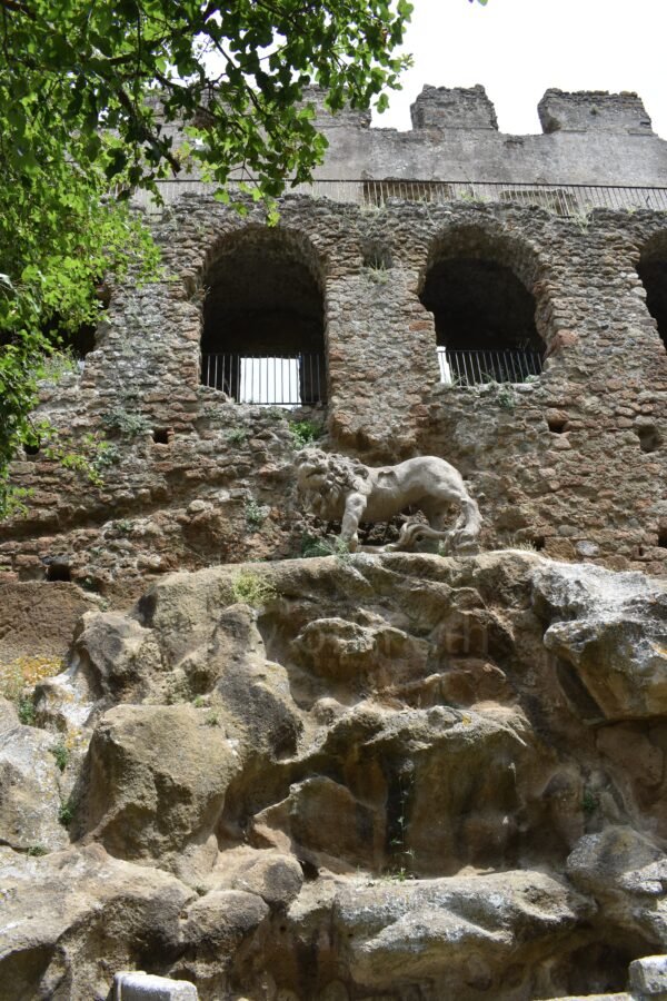Stone lion fountain set into the rocky facade of the Ducal Palace ruins in Antica Monterano ghost town, Lazio, Italy.