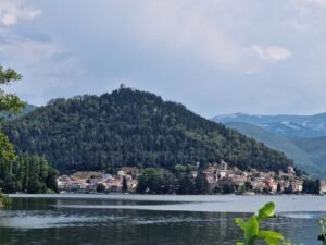View across Lake Piediluco toward the village at the base of the forested hill with the Rocca Albornoziana ruins at the peak, Umbria, Italy.