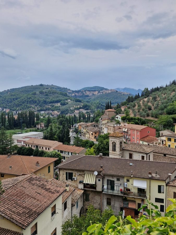 Rooftops of the lower village in Arrone looking out over the Valnerina valley toward olive-covered hills and a distant hilltop town, Umbria, Italy