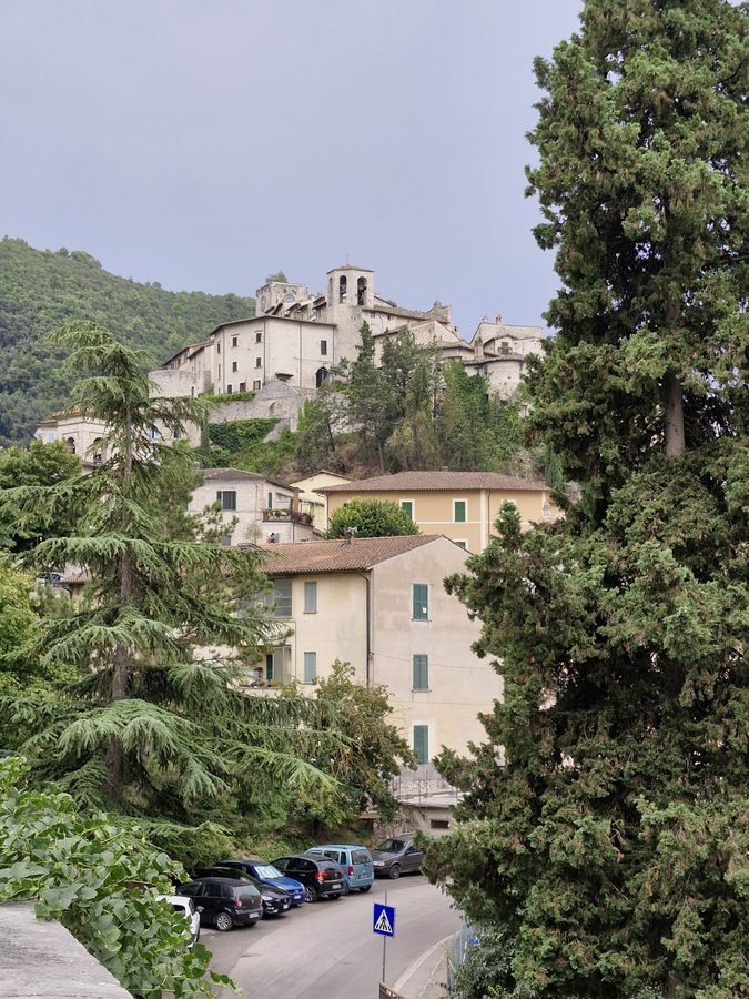Medieval stone houses and the bell tower of Arrone perched on a steep hill above modern buildings and parked cars, Umbria, Italy.