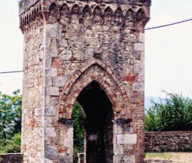 An ancient stone and brick gate tower with medieval features in Frosini, Tuscany, featuring a crenellated top and a Gothic pointed archway.