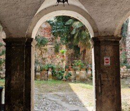 Stone-paved vaulted passageway framing an internal courtyard with potted plants, stone walls, and greenery in Narni, Umbria.