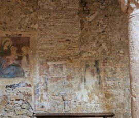 Faded medieval frescoes on exposed stone and brick masonry behind a wooden bench inside a church in Narni, Umbria.