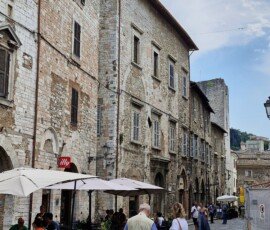 Paved street lined with weathered stone townhouses, outdoor café seating, and pedestrians in the historic center of Narni, Umbria.