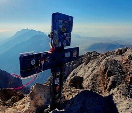 Summit cross covered in stickers and ribbons at the top of Corno Grande overlooking the rugged mountain ridge and surrounding valleys in Gran Sasso, Abruzzo, Italy.