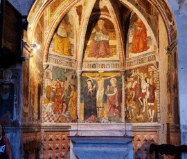 Stone altar beneath an apse decorated with Renaissance frescoes showing the Crucifixion and saints inside the Church of San Giovanni Battista in Arrone, Umbria, Italy
