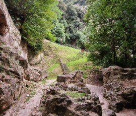 Rocky walking trail leading toward wooden stairs and fenced paths on a steep green hillside near Ponte del Toro, Umbria.