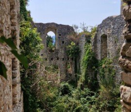 Crumbling stone walls and arched window openings overtaken by vegetation inside the Rocca Albornoz fortress ruins, Umbria, Italy.