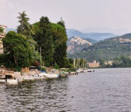 Small boats moored along the tree-lined shore of Lake Piediluco with the hilltop village of Labro visible in the distance.