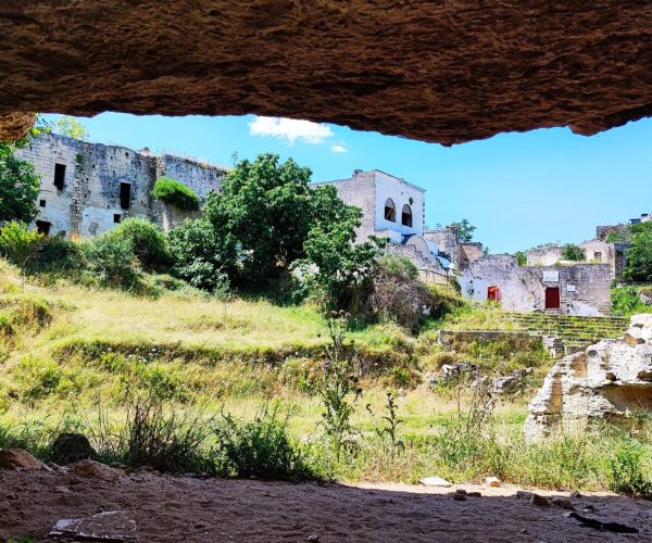The old white houses of Ginosa stand behind the trees and grassy area of ​​Gravina di Ginosa.