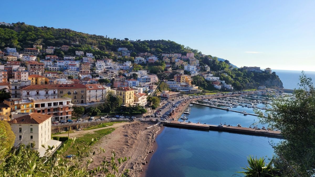 is Agropoli worth visiting. View of Agropoli on the Cilento Coast in Italy, with colorful hillside houses overlooking the marina, beach, and calm Tyrrhenian Sea on a clear sunny day.