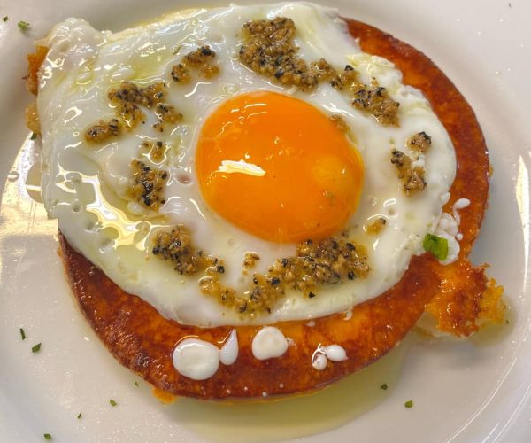 Where to eat in Castelpetroso Fried egg with a bright orange yolk served on top of a crispy round slice of fried cheese, garnished with minced garlic and herbs.
