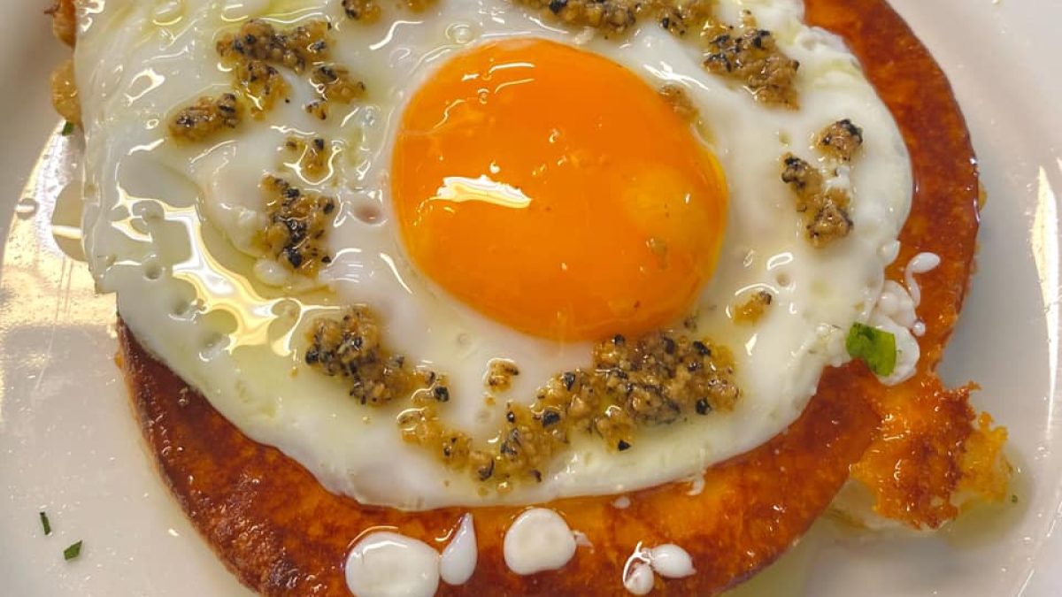 Where to eat in Castelpetroso Fried egg with a bright orange yolk served on top of a crispy round slice of fried cheese, garnished with minced garlic and herbs.