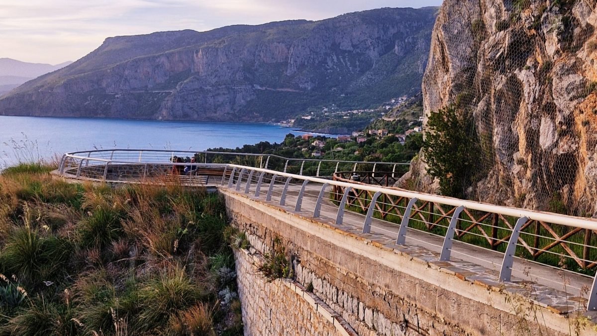 Stone skywalk pathway with metal railings built along a rocky cliffside, overlooking the sea and coastline in Maratea, Basilicata, Italy.
