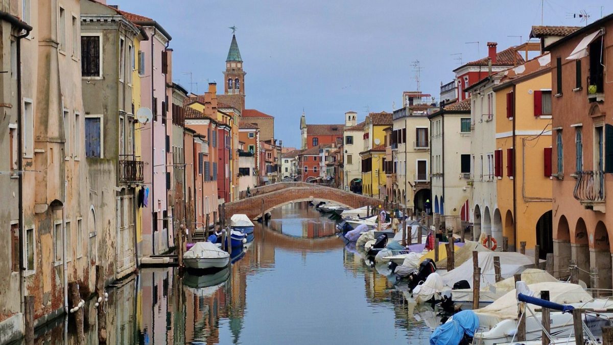 Visiting Chioggia. A water canal in Chioggia lined with multi-colored houses and moored boats under an overcast sky